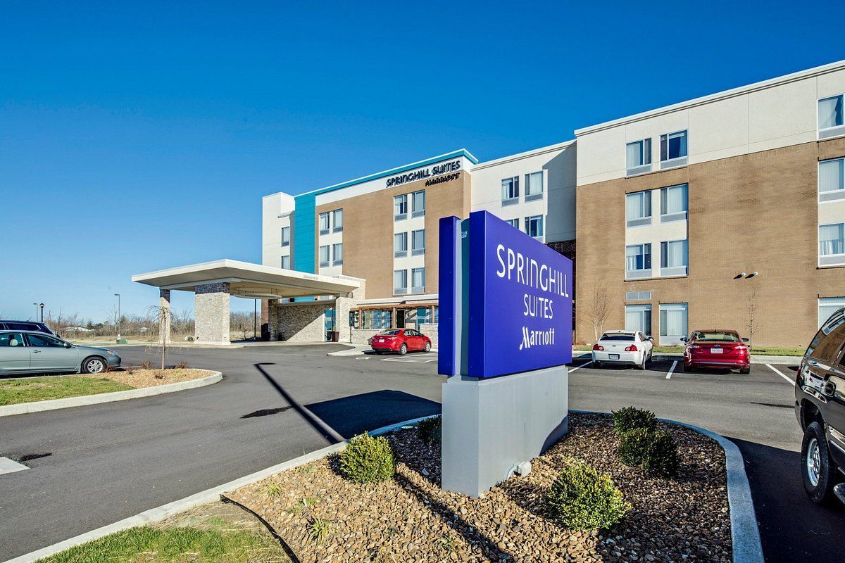 A hotel with a purple sign in front of it and cars parked in front of it.