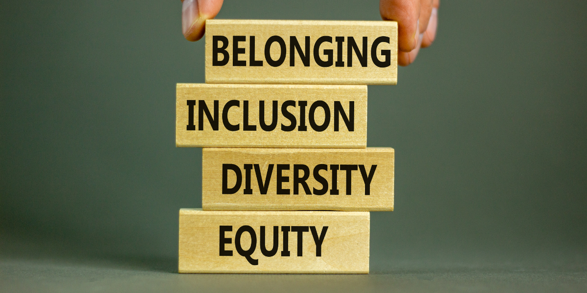 A person is holding wooden blocks with the words belonging inclusion diversity equity written on them.