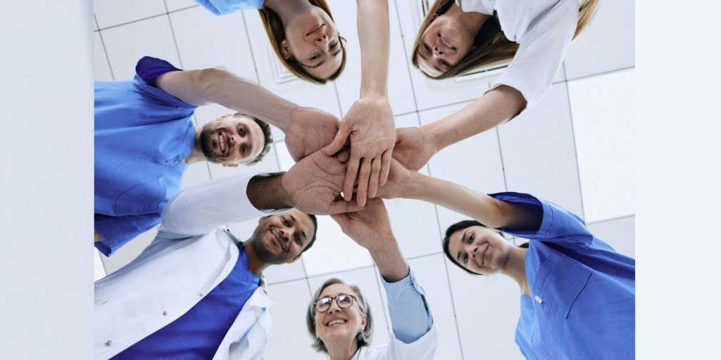 A group of doctors and nurses are putting their hands together in a circle.