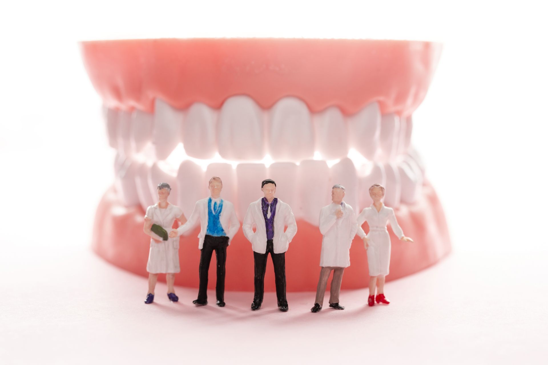 A group of miniature dentists standing next to a model of teeth.