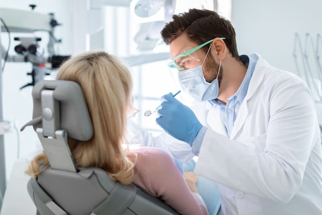 A dentist is examining a woman 's teeth in a dental office.