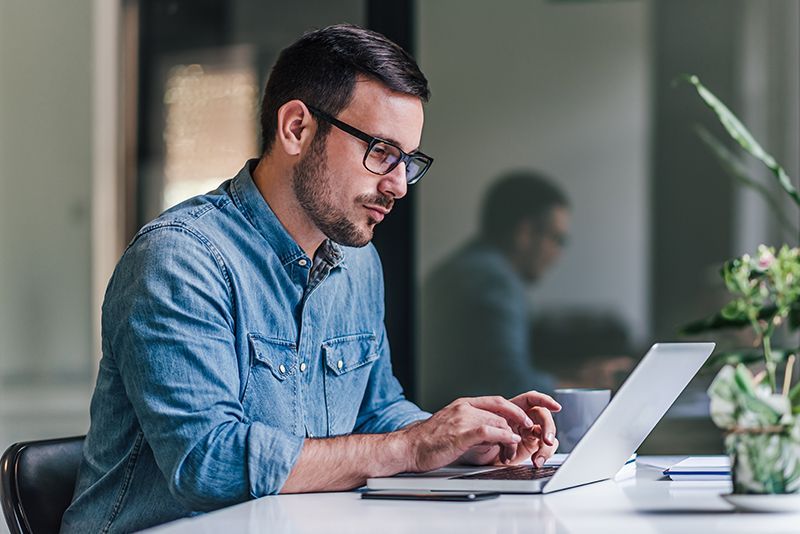 A man is sitting at a table using a laptop computer.