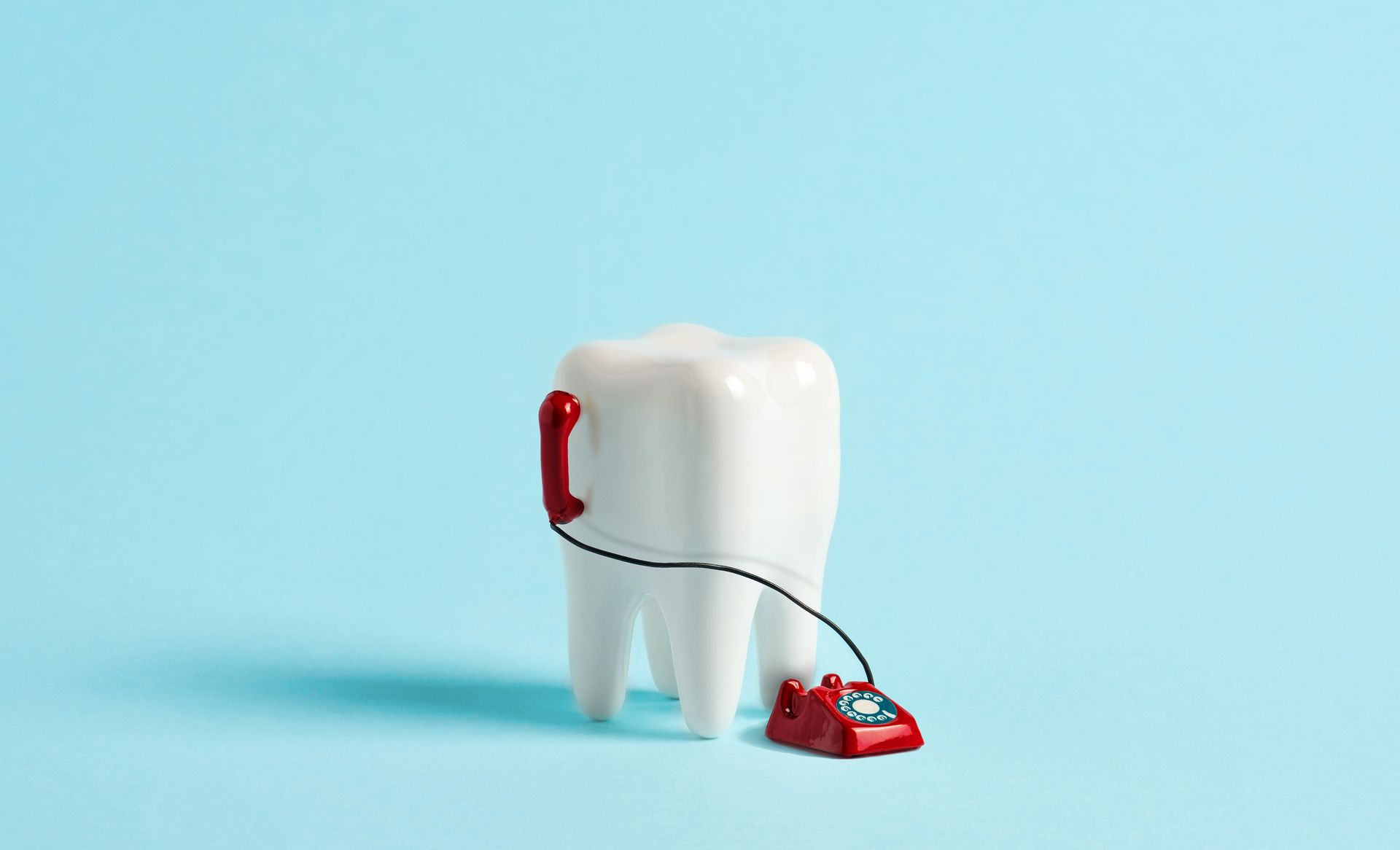 A tooth is connected to a red telephone on a blue background.