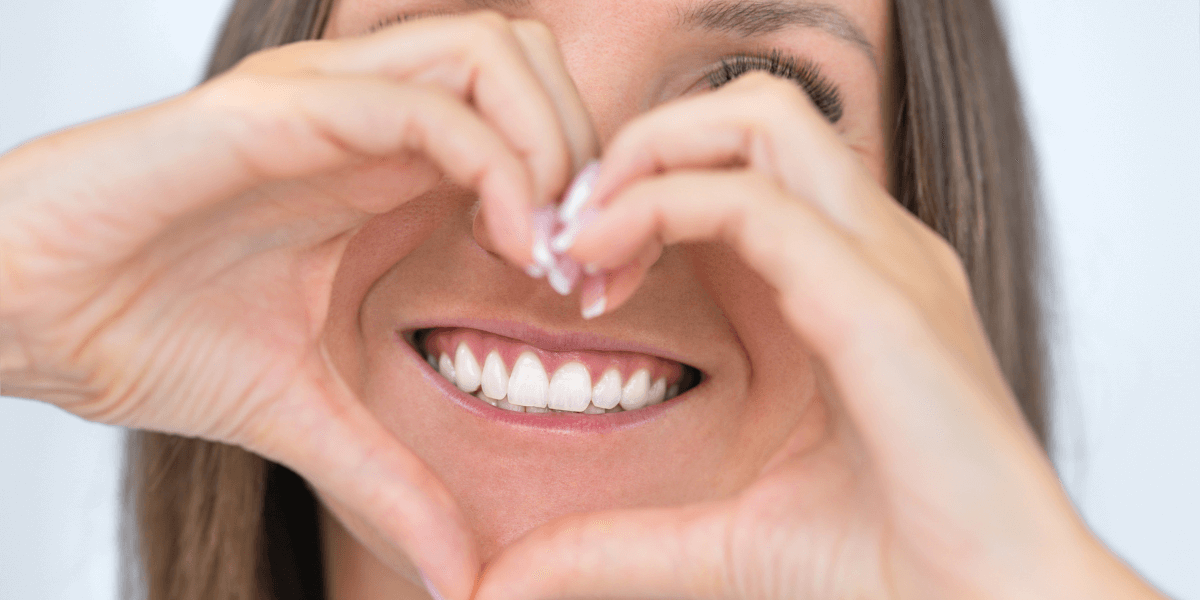 A woman is making a heart shape with her hands over her mouth.
