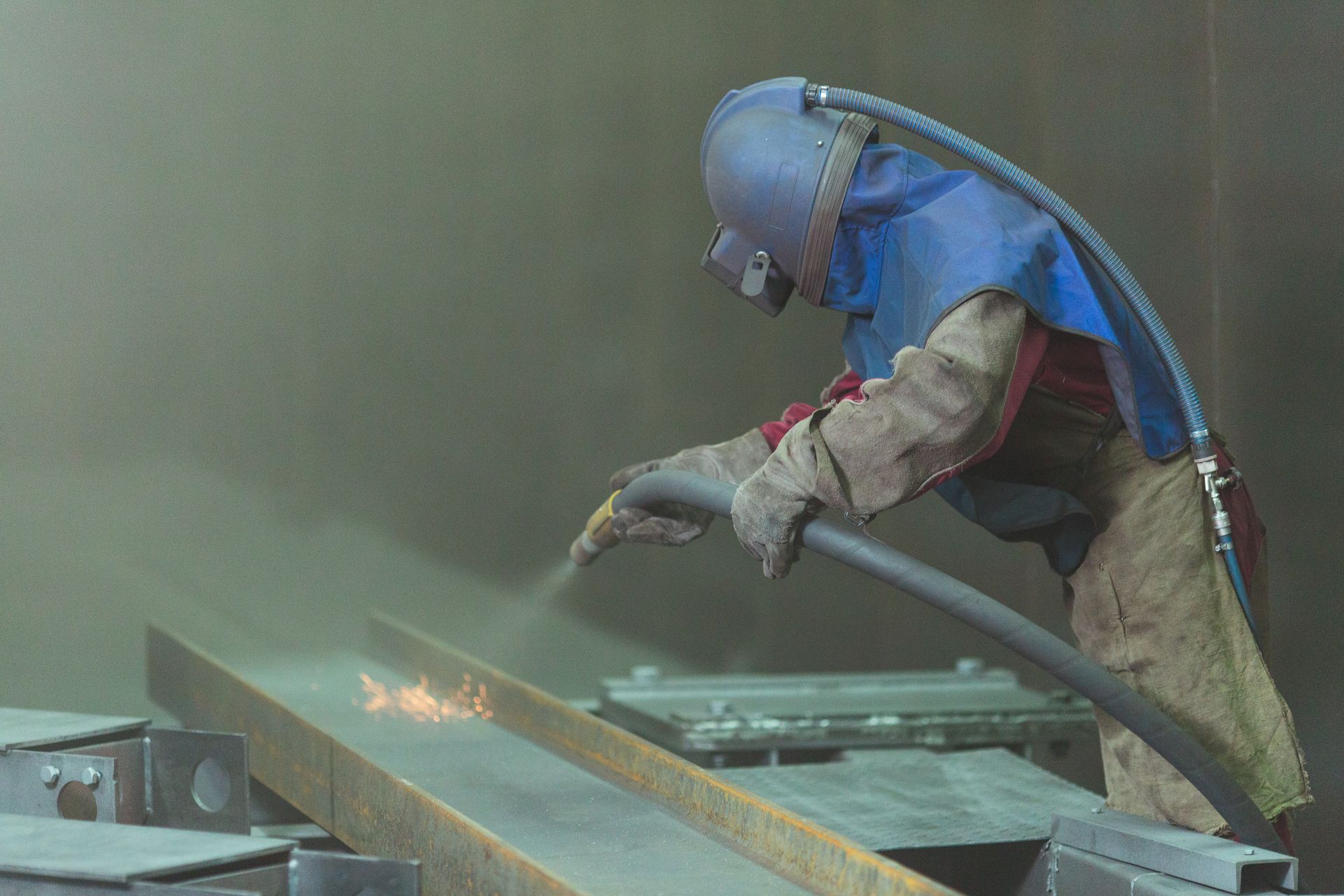 A man is sandblasting a piece of metal