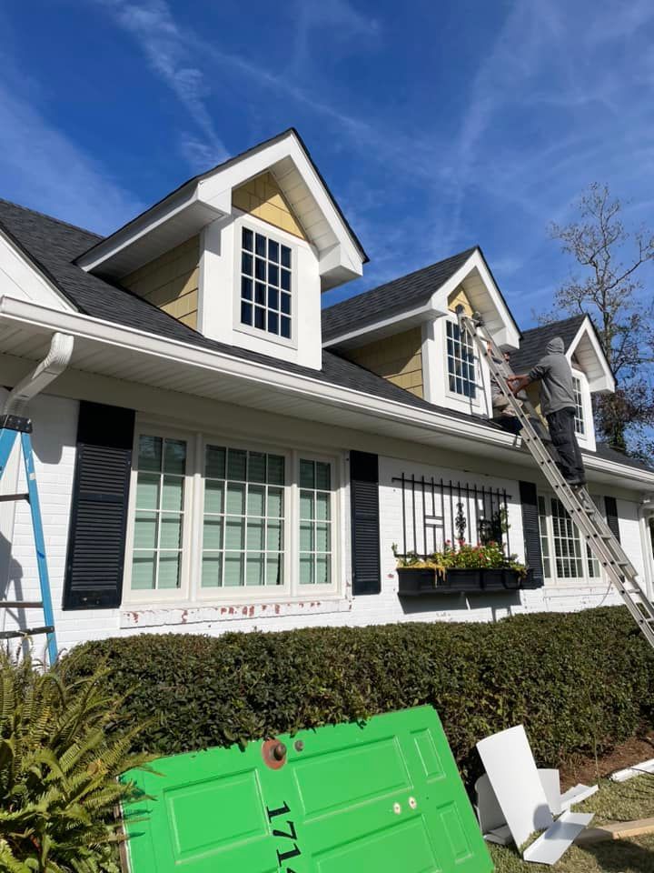A man is painting the roof of a house with a ladder.