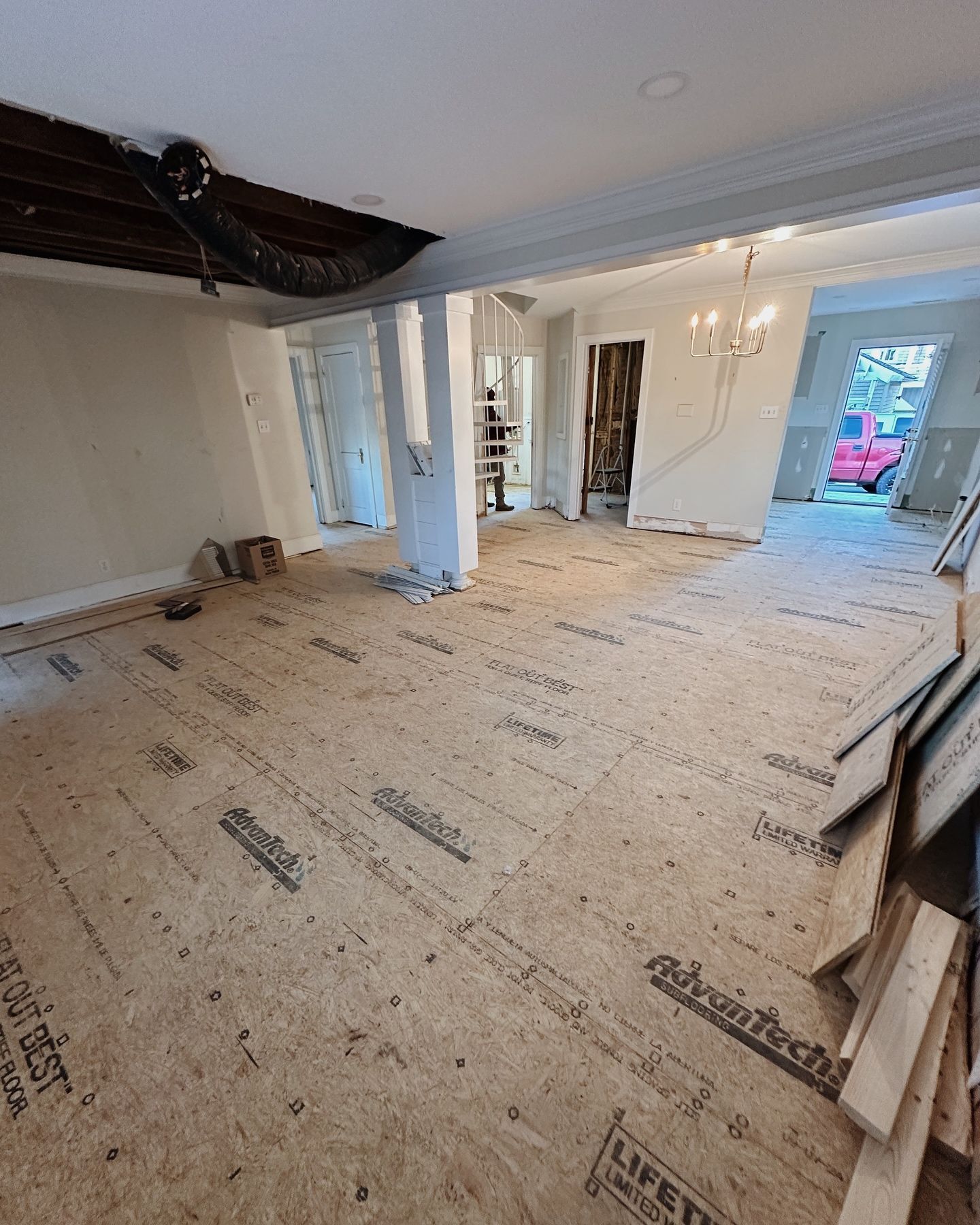 A large empty room with a wooden floor and a red car parked in the background.