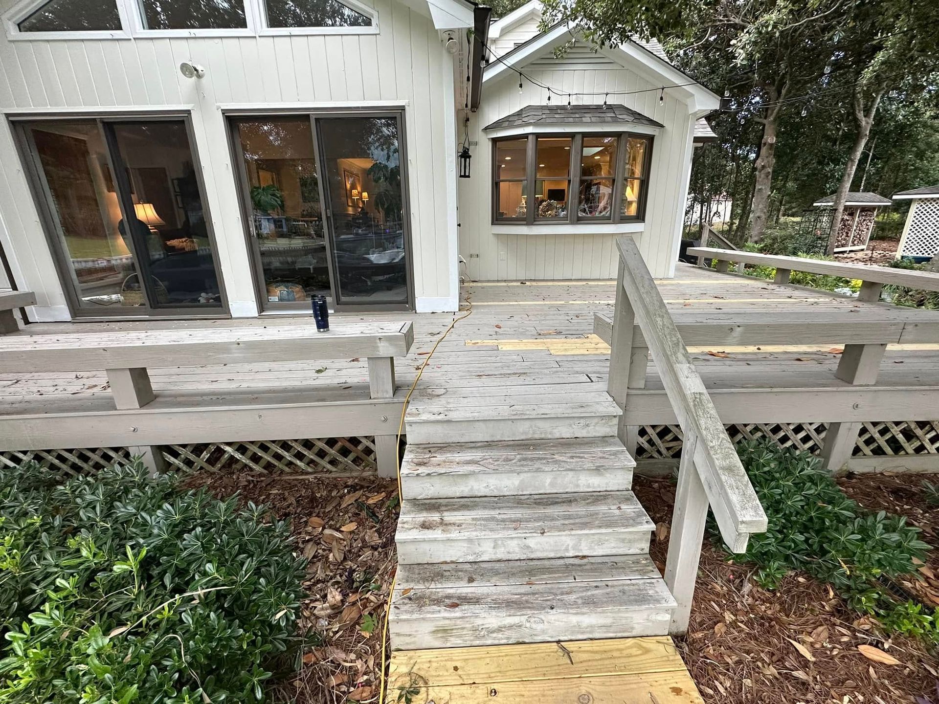 A white house with a wooden deck and stairs leading to it.