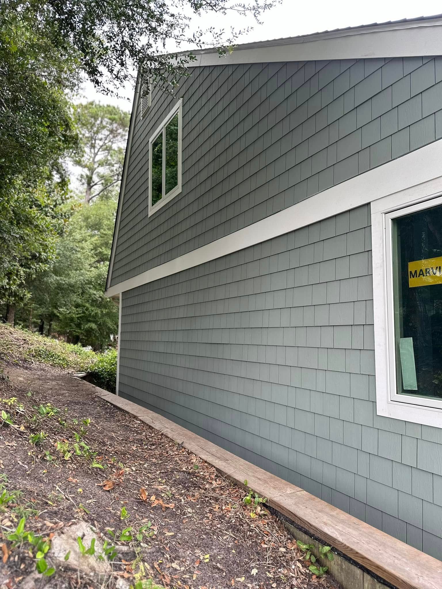 A house with a gray siding and white trim is sitting on top of a hill.