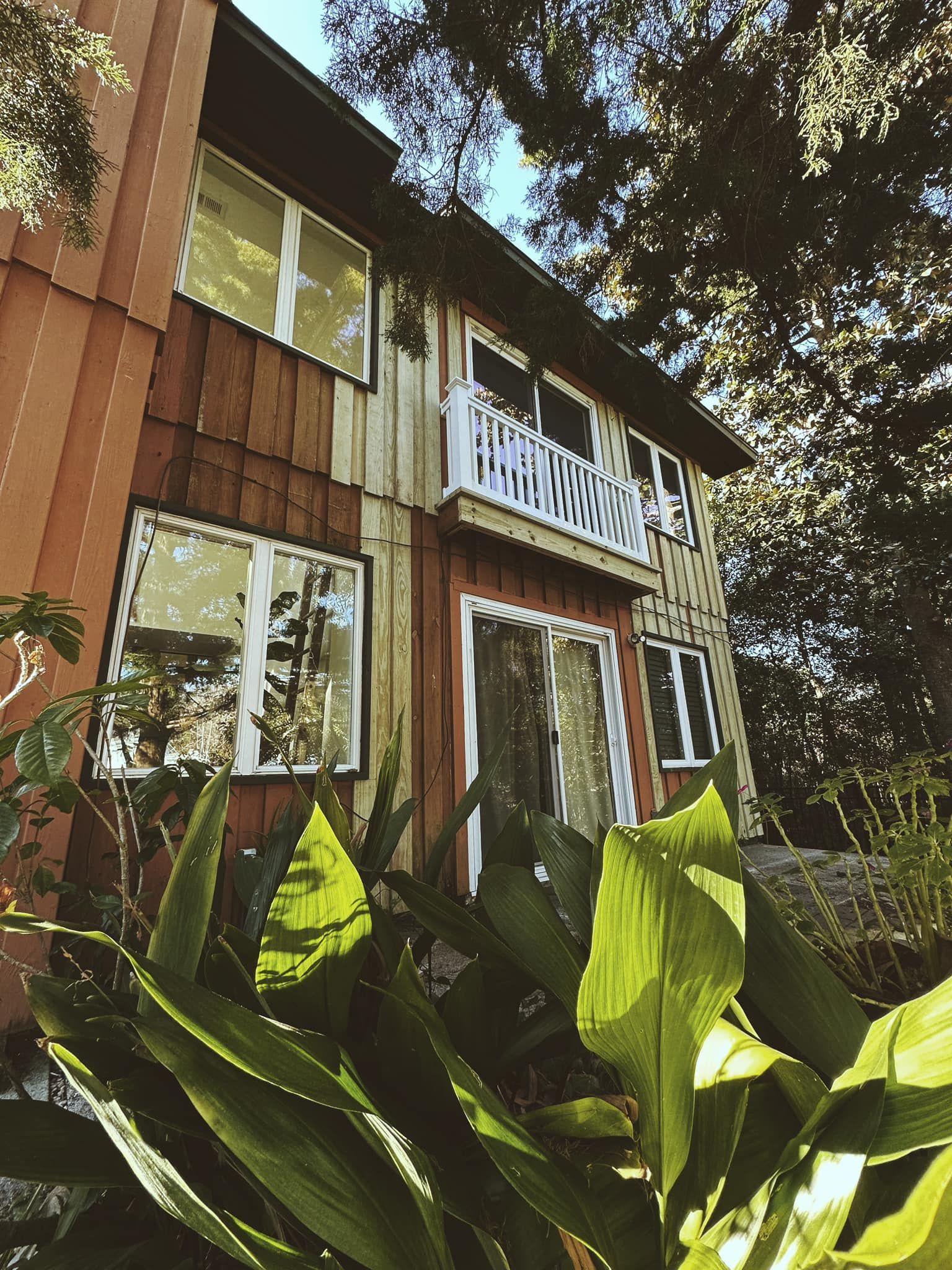 A house with a balcony is surrounded by trees and plants.