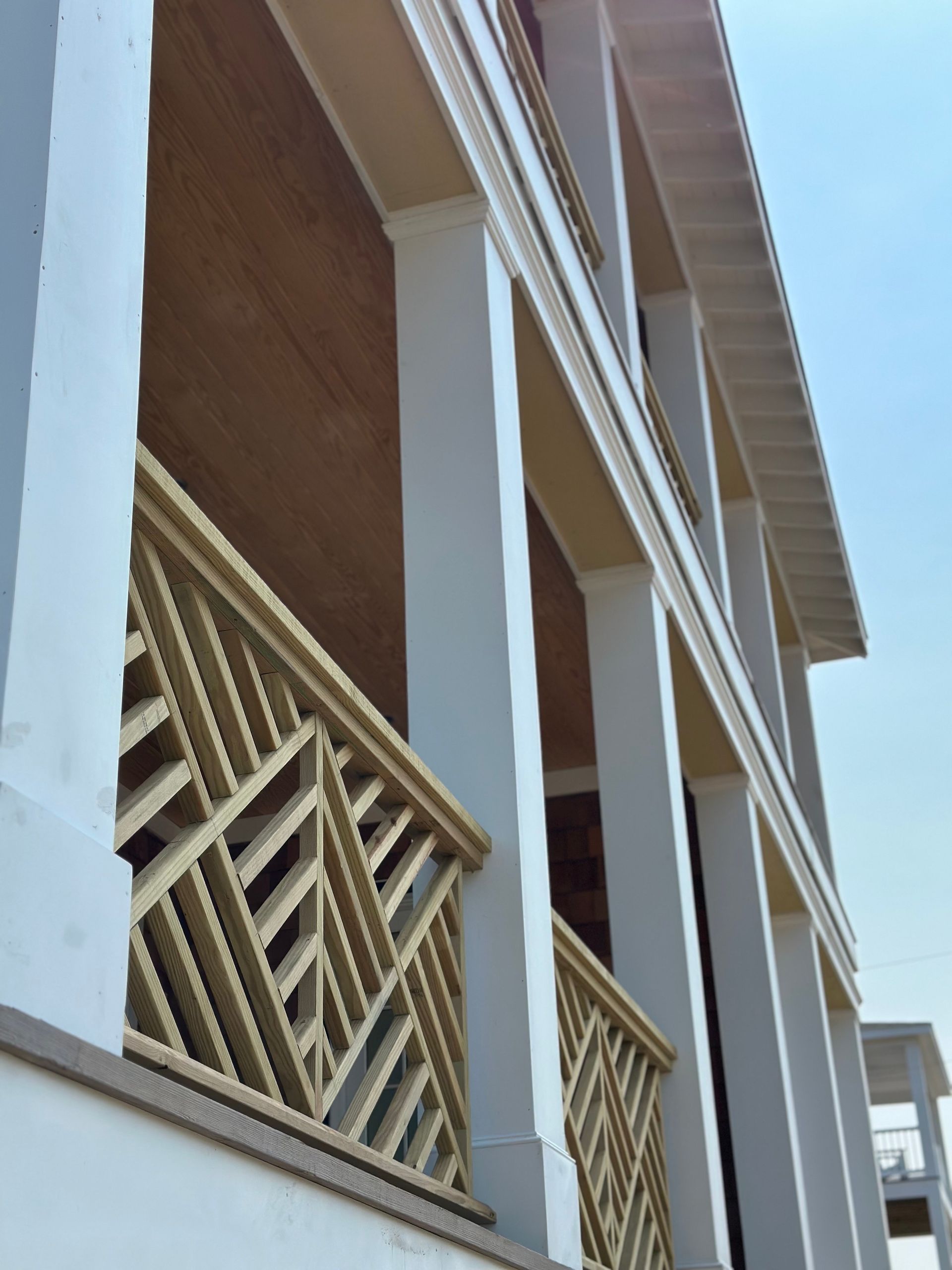 Beige and white building facade with decorative railing and columns against a clear sky.