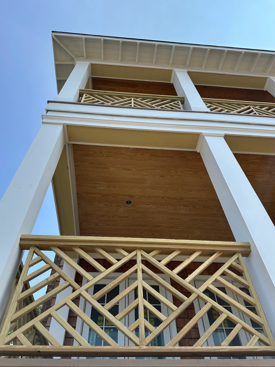 Two-story building with light brown and white exterior, intricate balcony railings, against a blue sky.