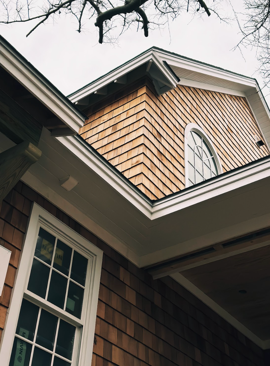House exterior with wood shingle siding and arched window. White trim, cloudy sky.