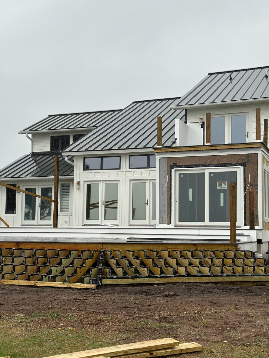 House under construction with a deck. White siding, gray roof, brown deck supports. Overcast sky.