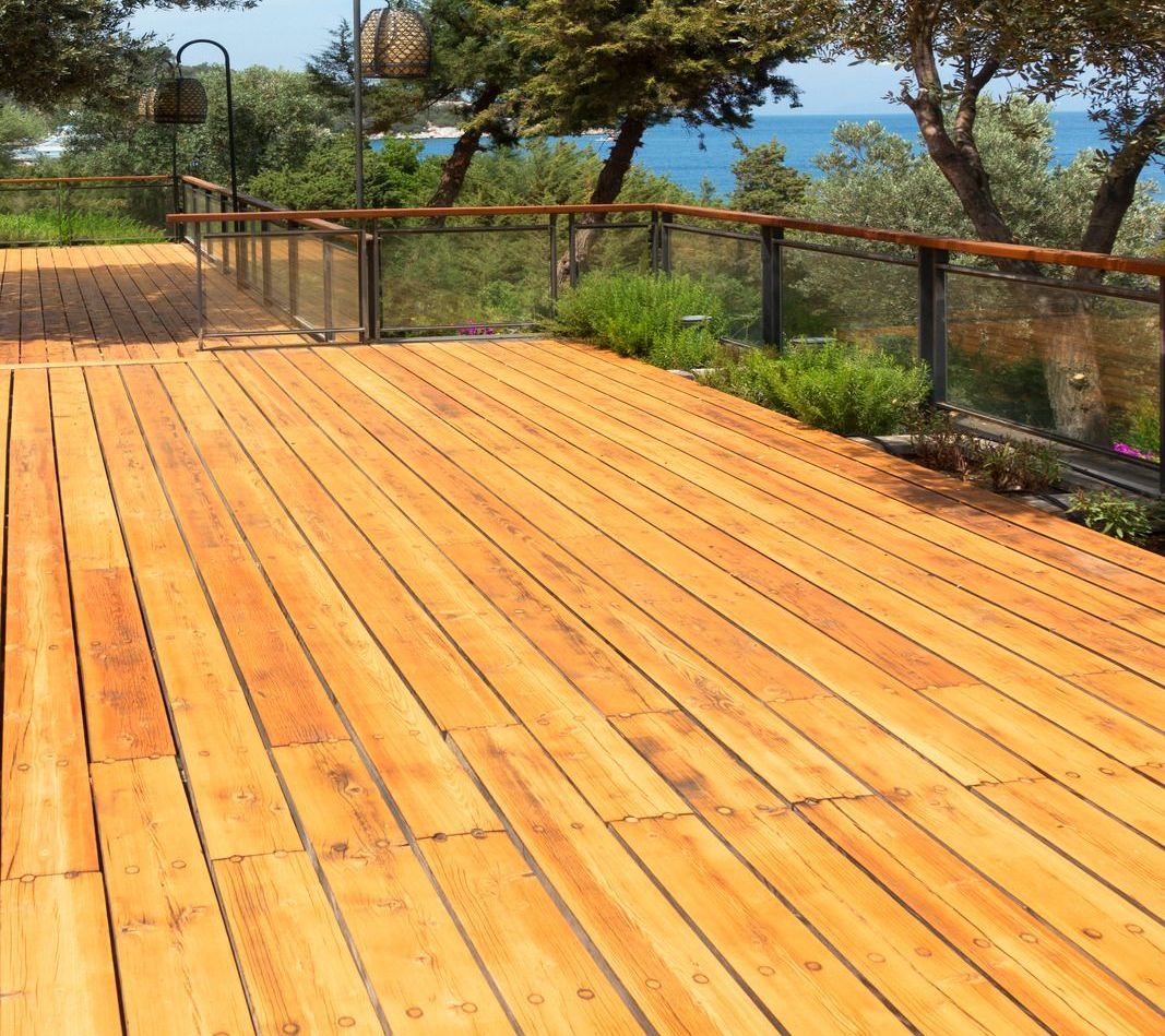 A wooden deck with a glass railing overlooking the ocean