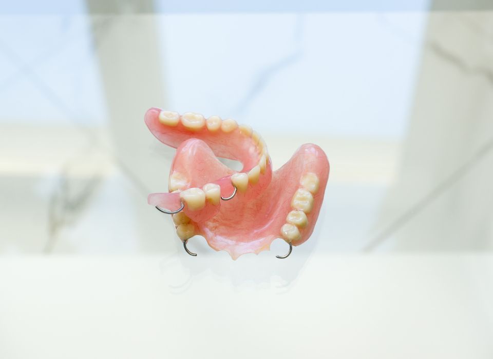 Set of upper and lower dentures, pink with white teeth, on a white surface.