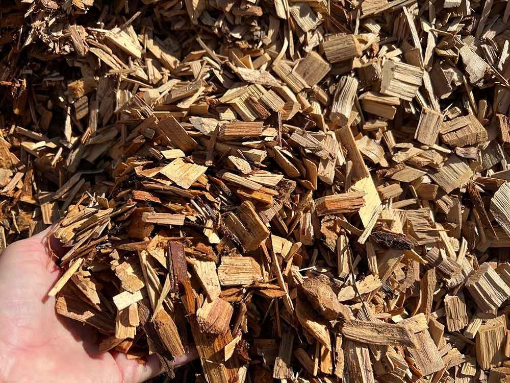 A Person Is Holding A Pile Of Wood Chips In Their Hand — Cooroy Landscape Supplies and Garden Centre in Gympie, QLD