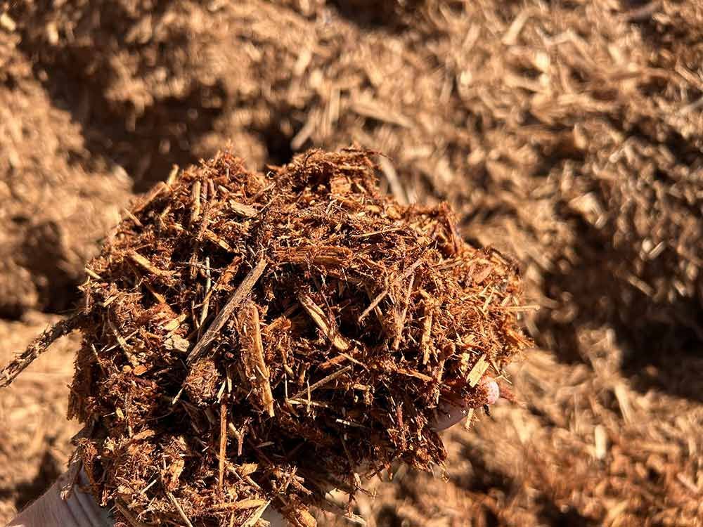 A Person Is Holding A Pile Of Wood Chips In Their Hand — Cooroy Landscape Supplies and Garden Centre in Noosa, QLD