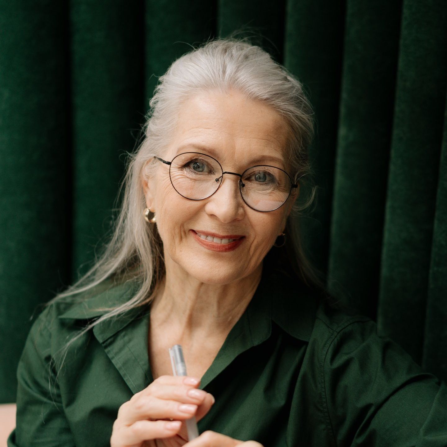 an older woman wearing glasses and a green shirt is holding a pen .