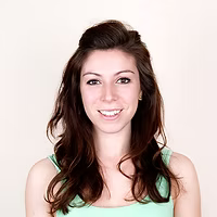 A woman with long brown hair is wearing a green tank top and smiling.