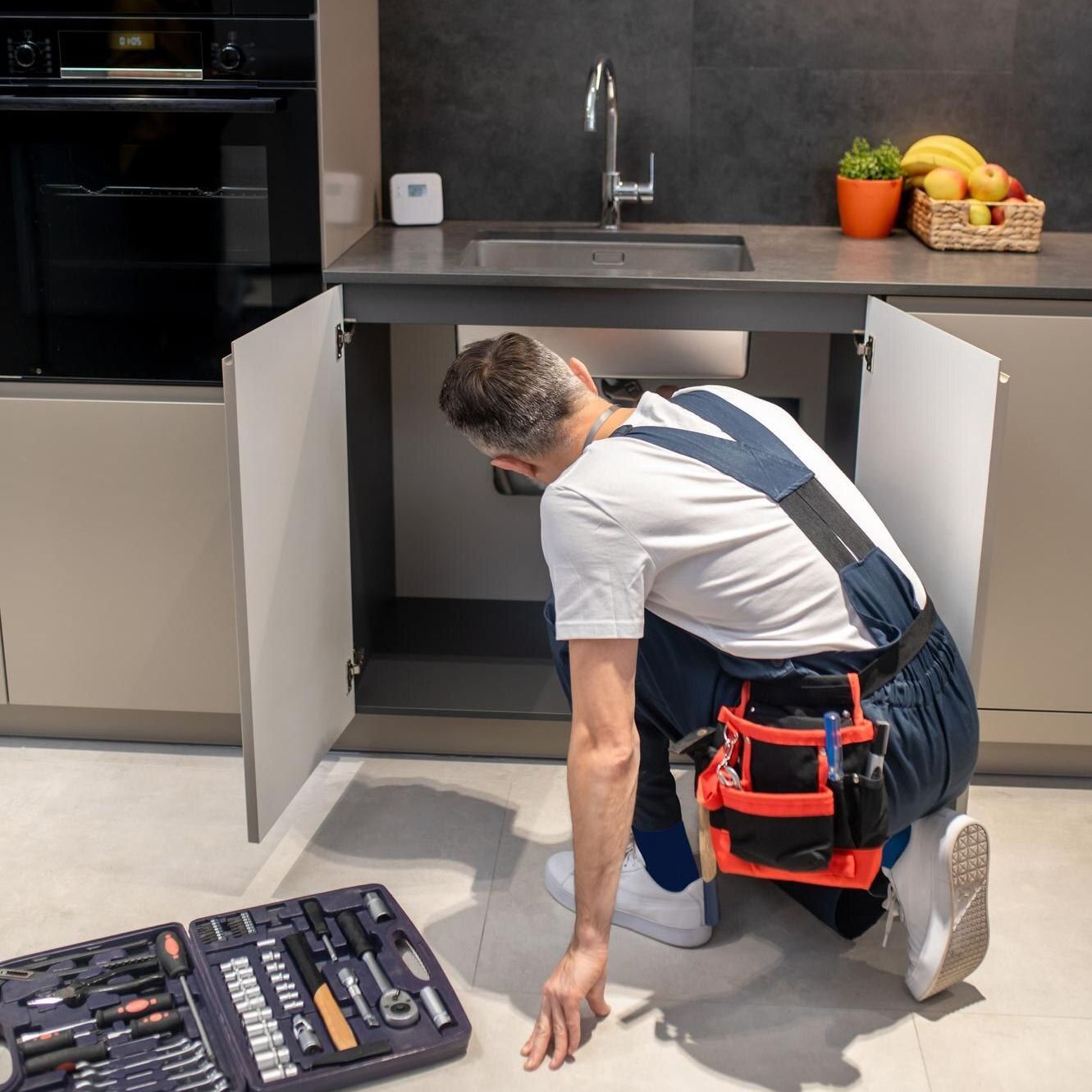 A man is working under a sink in a kitchen