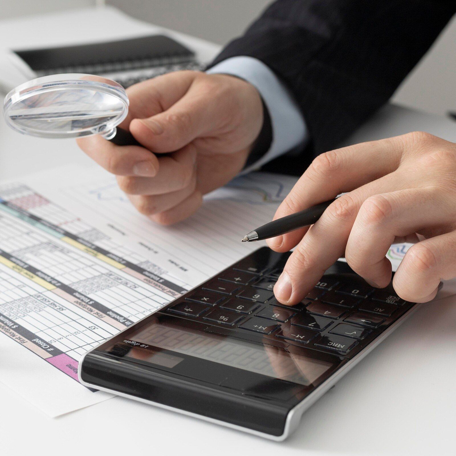 A person is holding a magnifying glass over a calculator