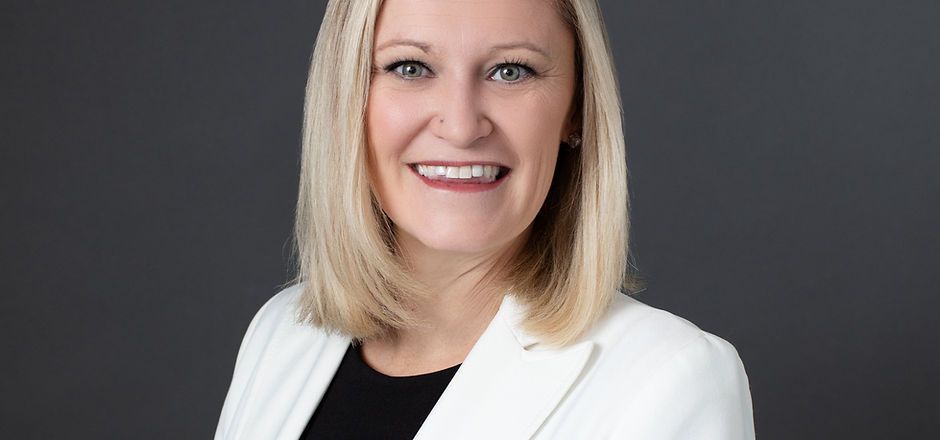 A woman in a white jacket and black shirt is smiling for the camera.
