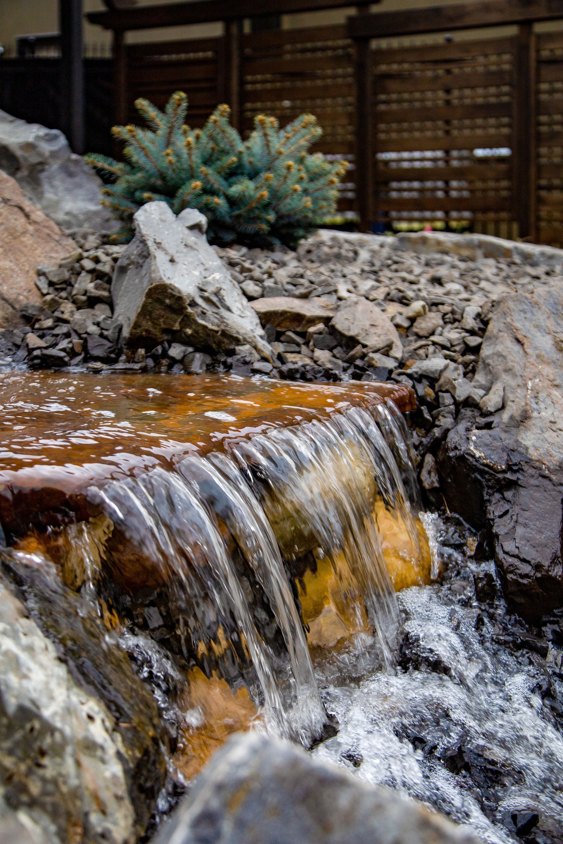 Small waterfall flowing over rocks beside a wooden fence and succulent plant