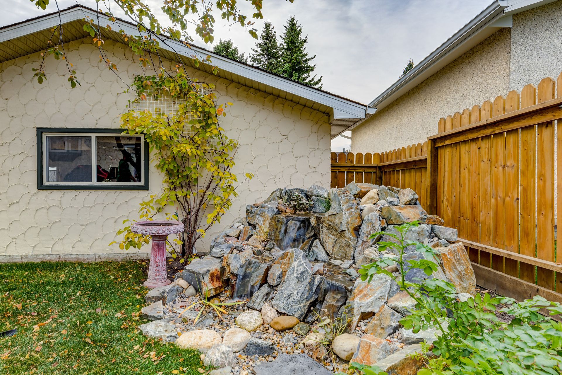 Backyard with rock waterfall feature, bird bath, and wooden fence.