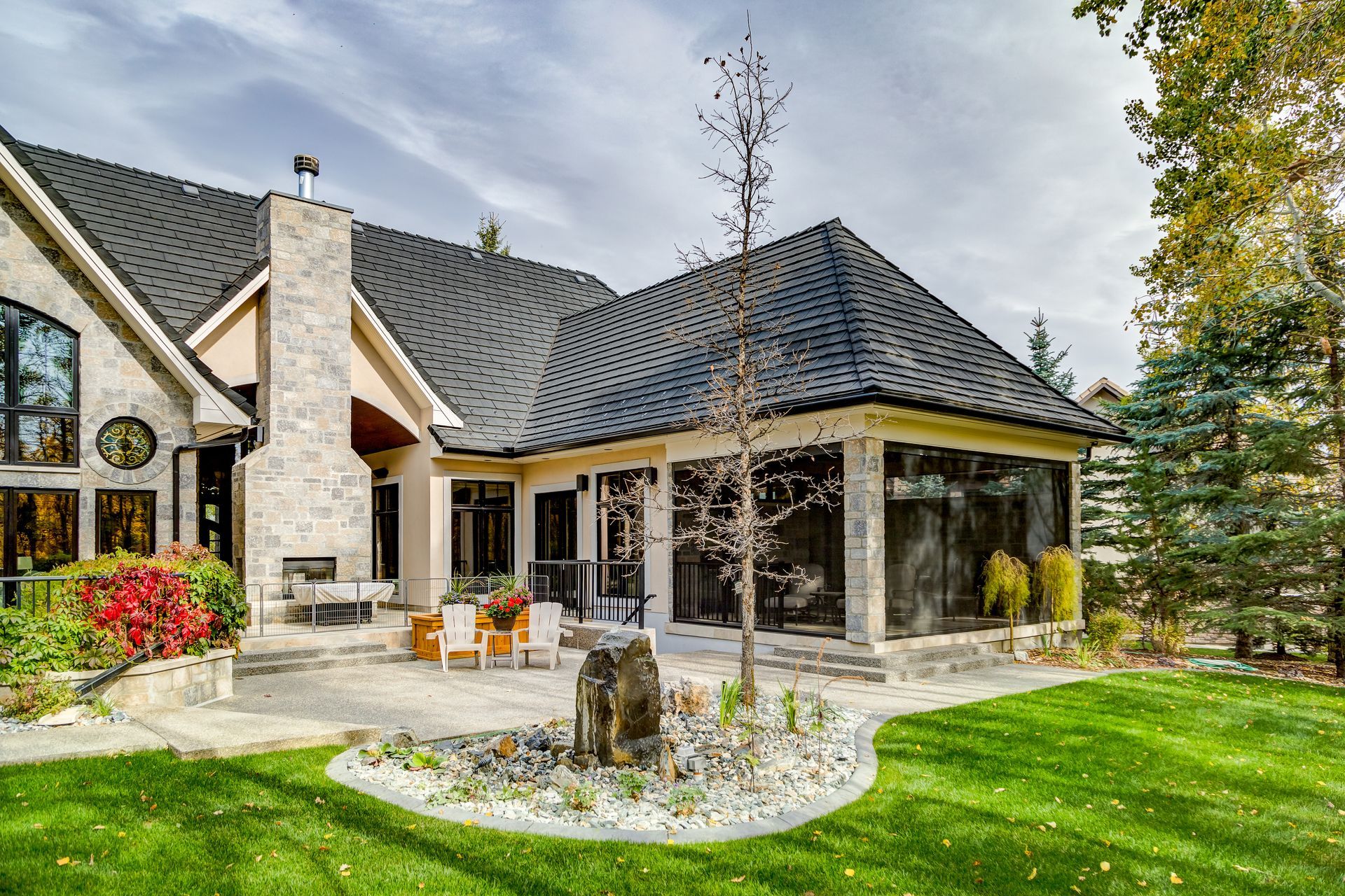 Backyard patio with stone facade, lawn, and a black roofed screened-in area.