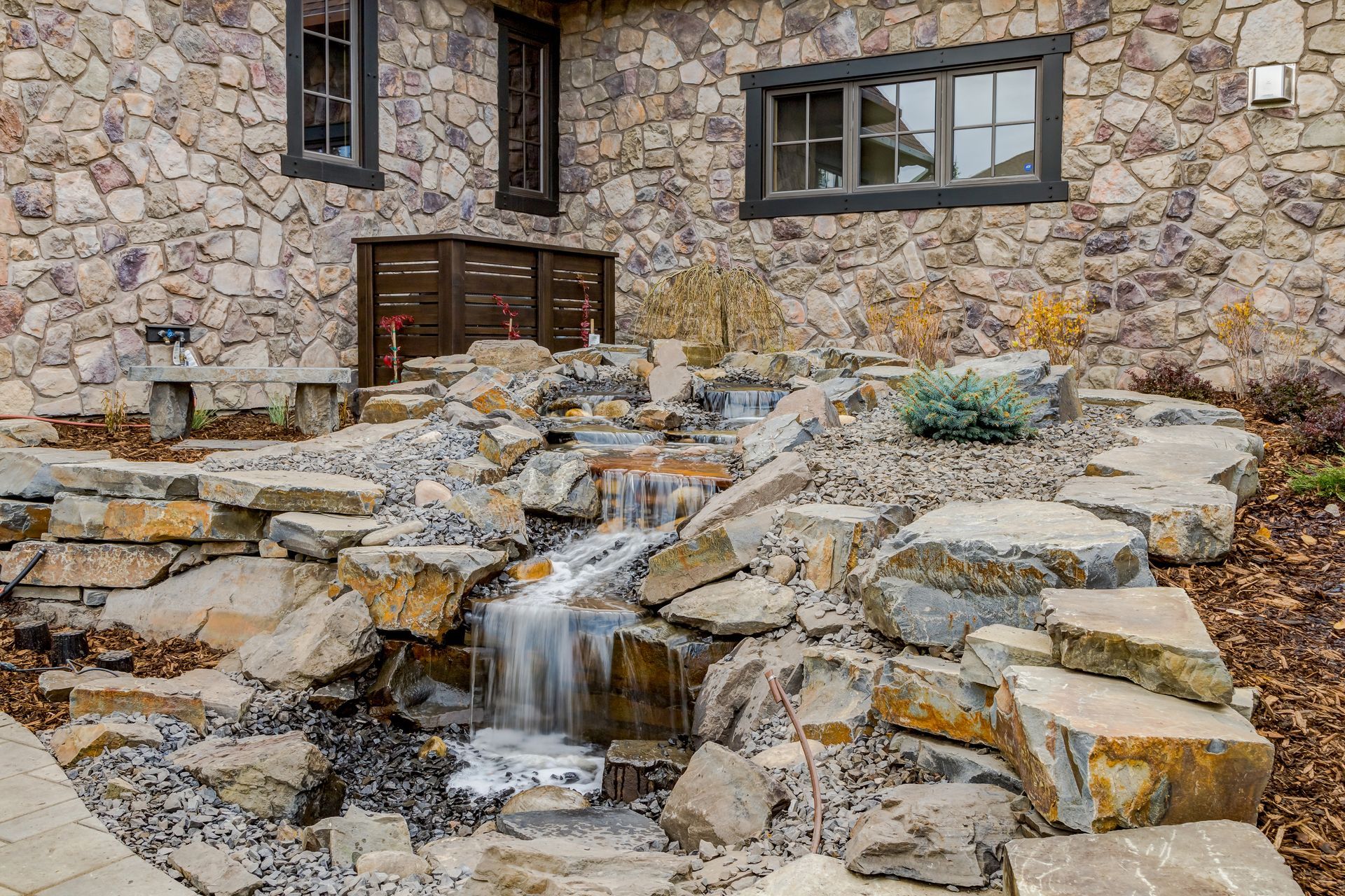 A waterfall is surrounded by rocks in front of a stone building.