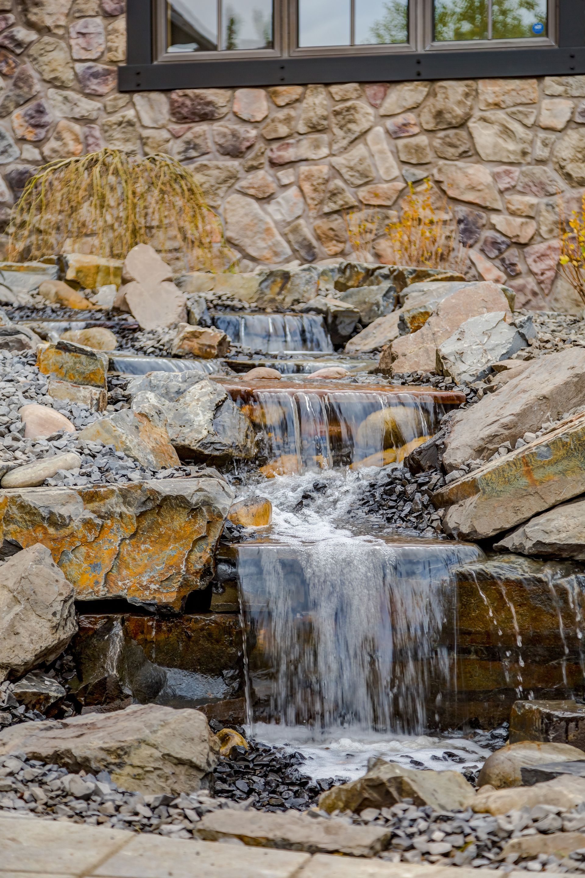 Water cascades down a stone waterfall feature in front of a stone building.