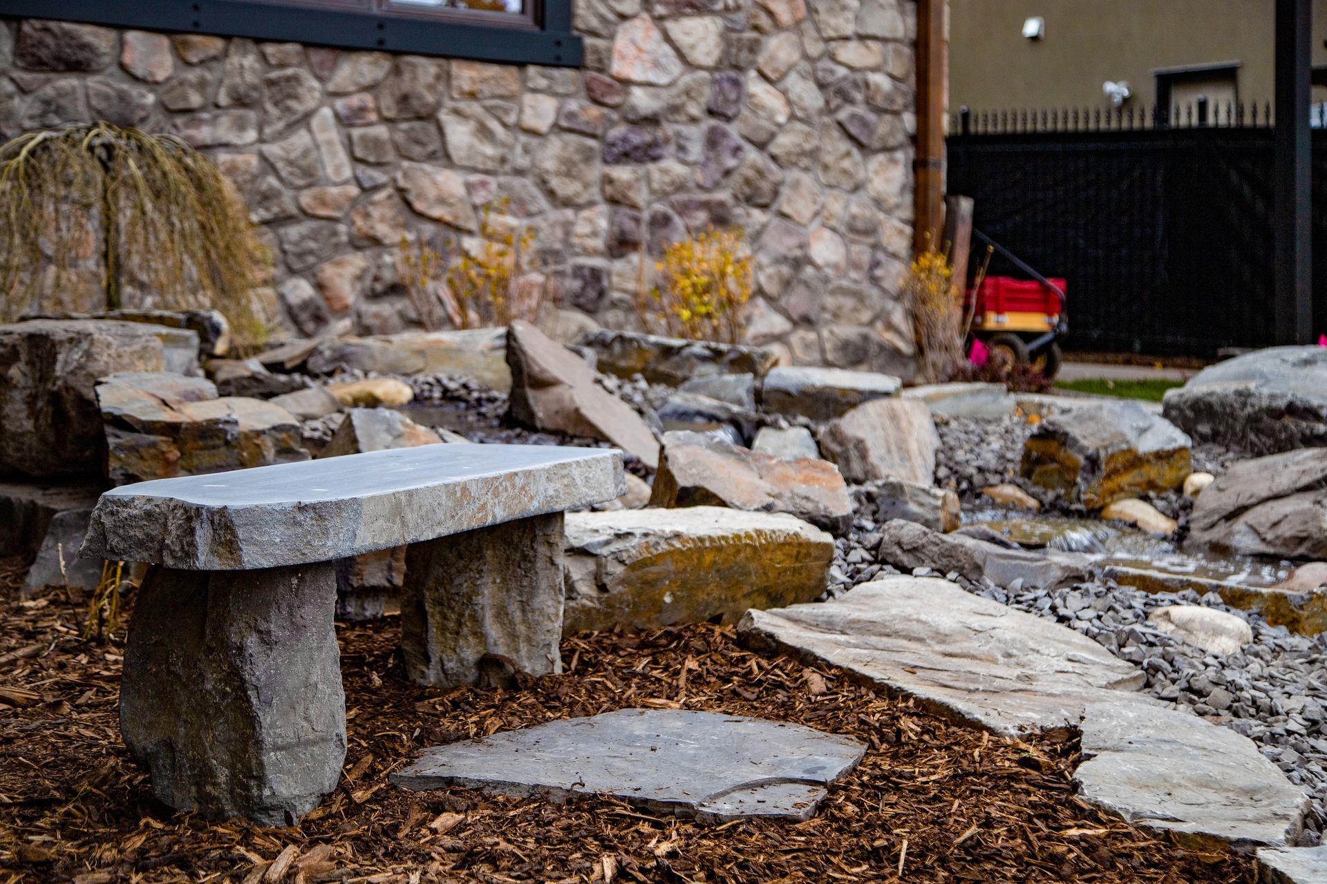 Stone bench and landscaped rock garden beside a stone wall and house exterior.