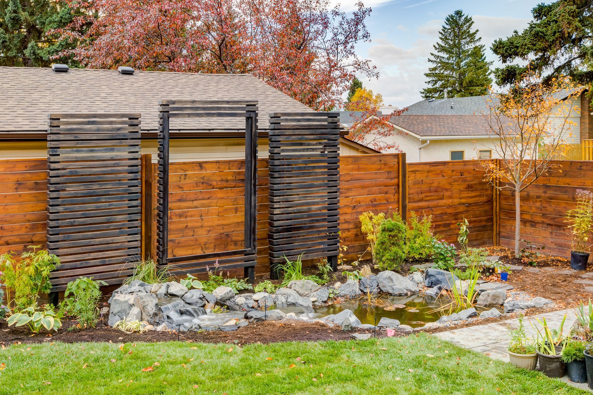 Backyard with wooden fence, garden pond, and decorative wood screens. Fall colors.