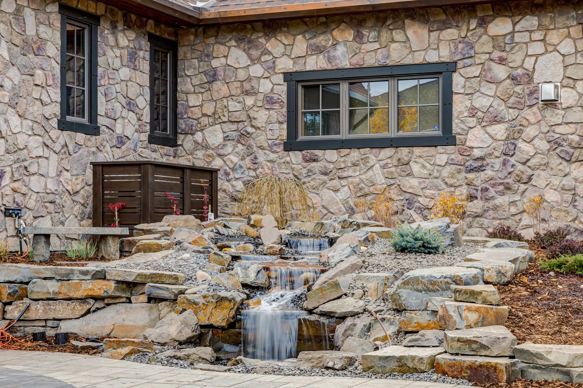 Stone facade with waterfall cascading down layered rock formations, near windows.