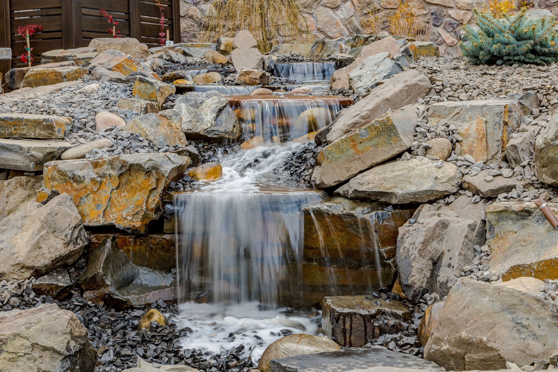 Water cascades down a rocky waterfall, surrounded by stones and vegetation.