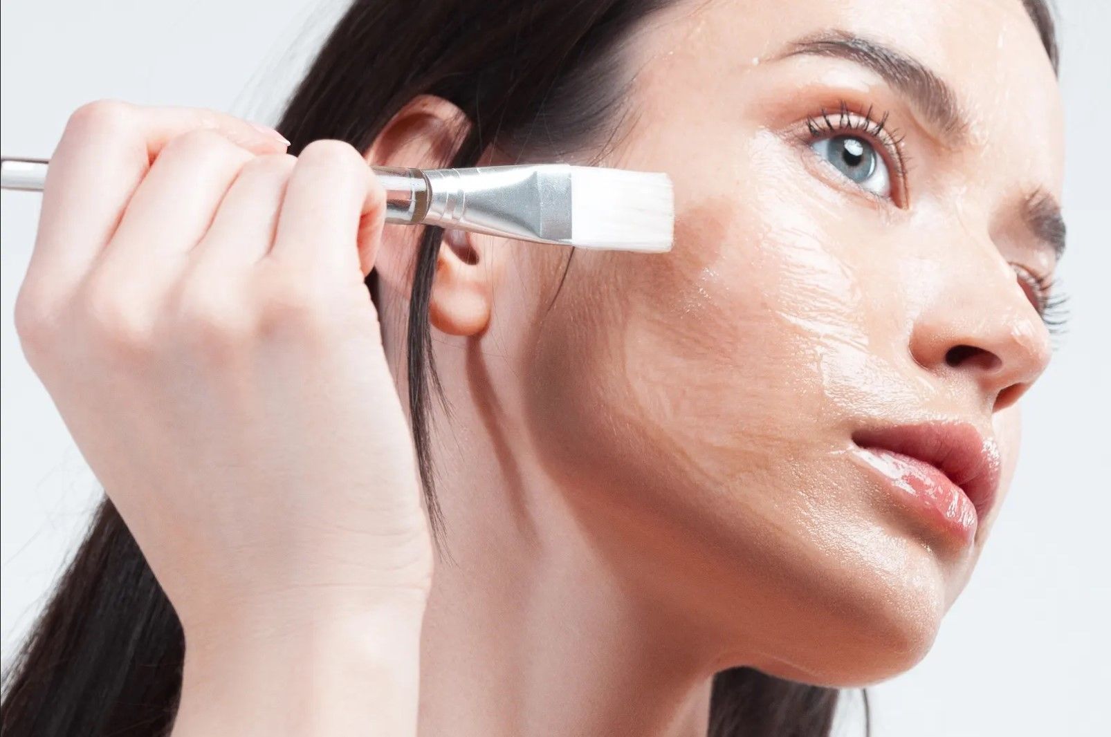 A woman is applying a mask to her face with a brush.