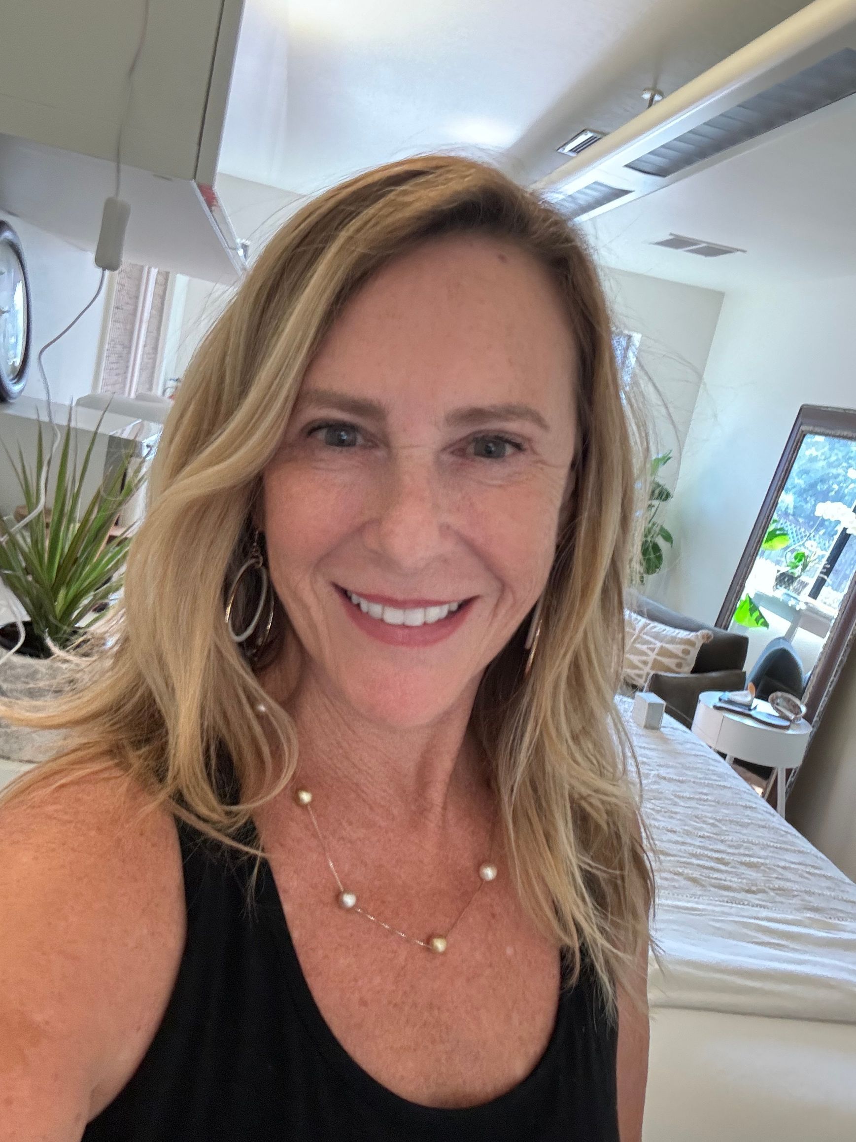 A woman in a black tank top and pearl necklace is smiling for the camera.
