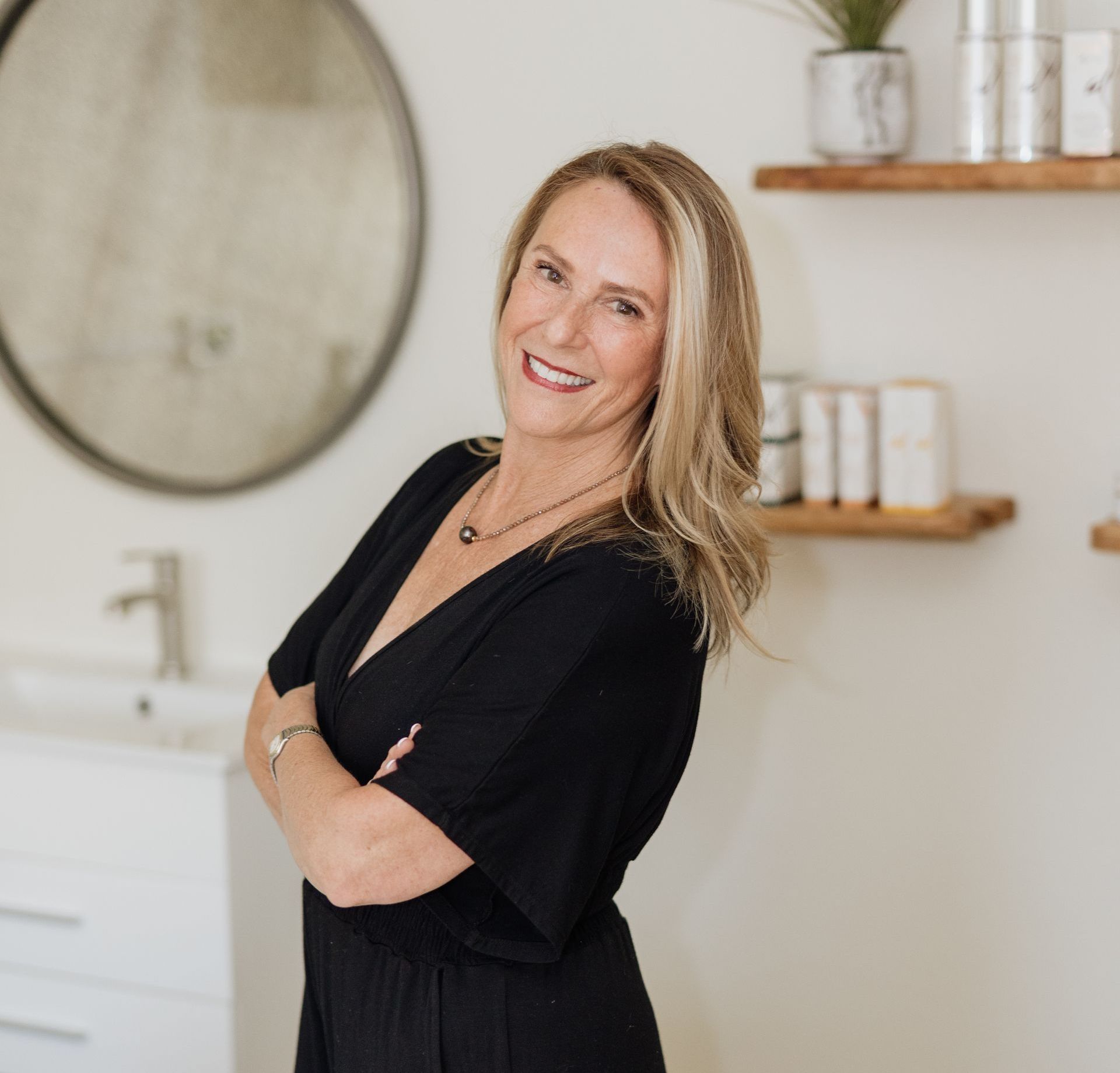 A woman in a black dress is smiling in front of a mirror