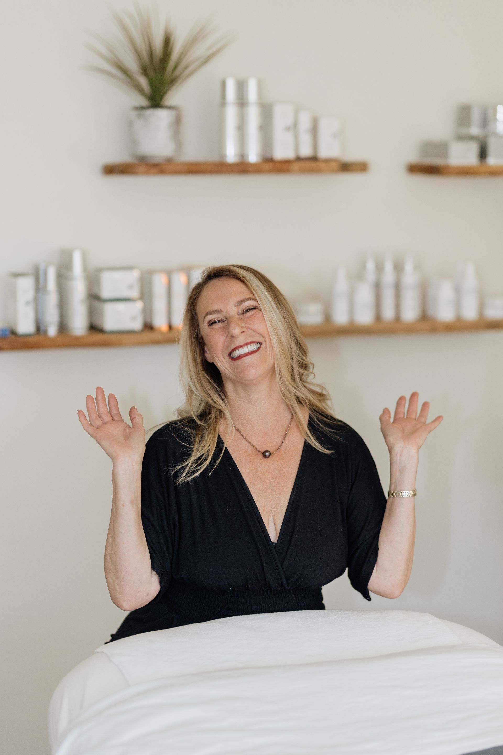 A woman in a black dress is sitting at a table with her arms outstretched.
