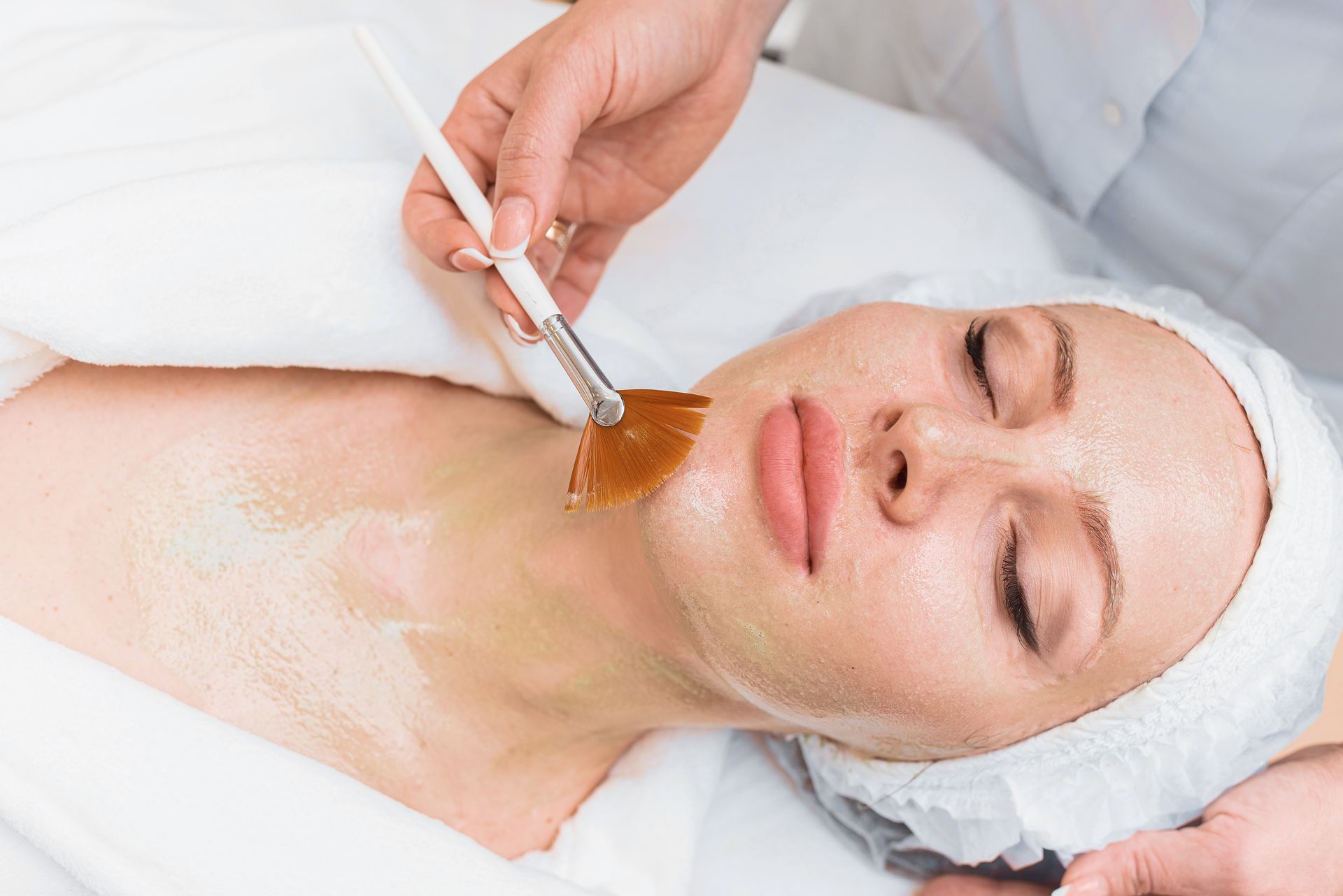 vPerson applying a facial mask with a brush to a woman's face at a spa.