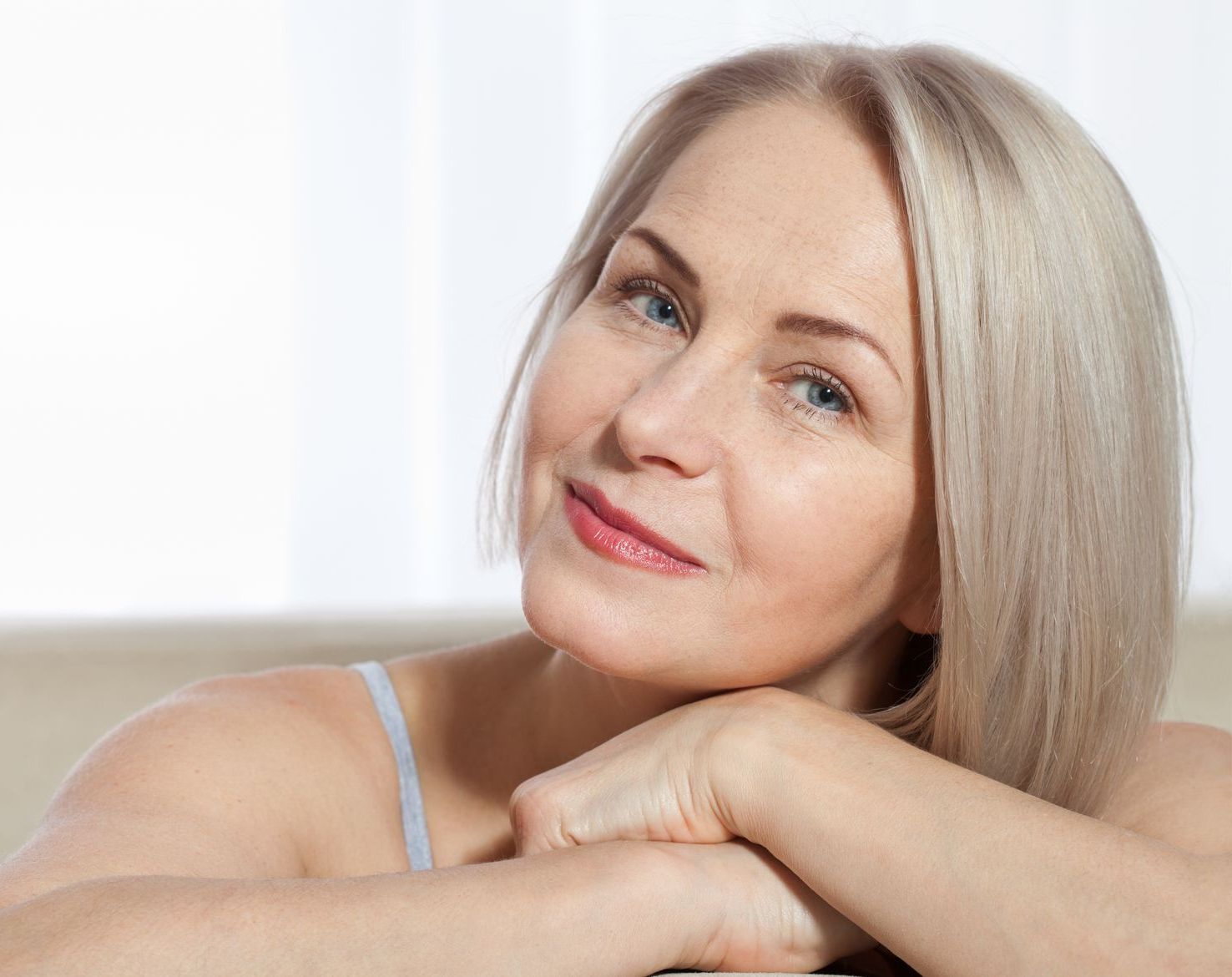 A woman is sitting on a couch with her hands on her face.