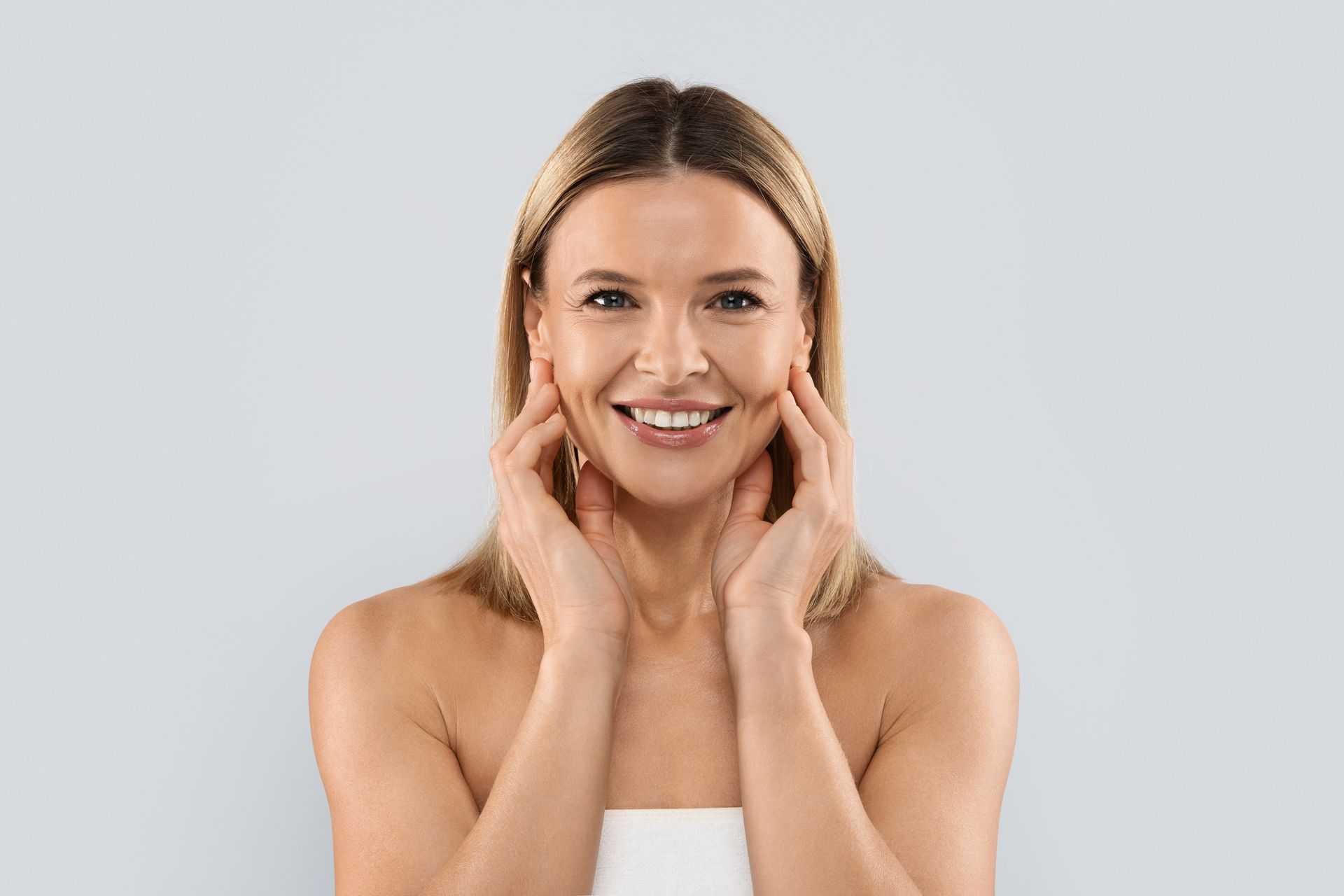 A woman is touching her face with her hands and smiling.