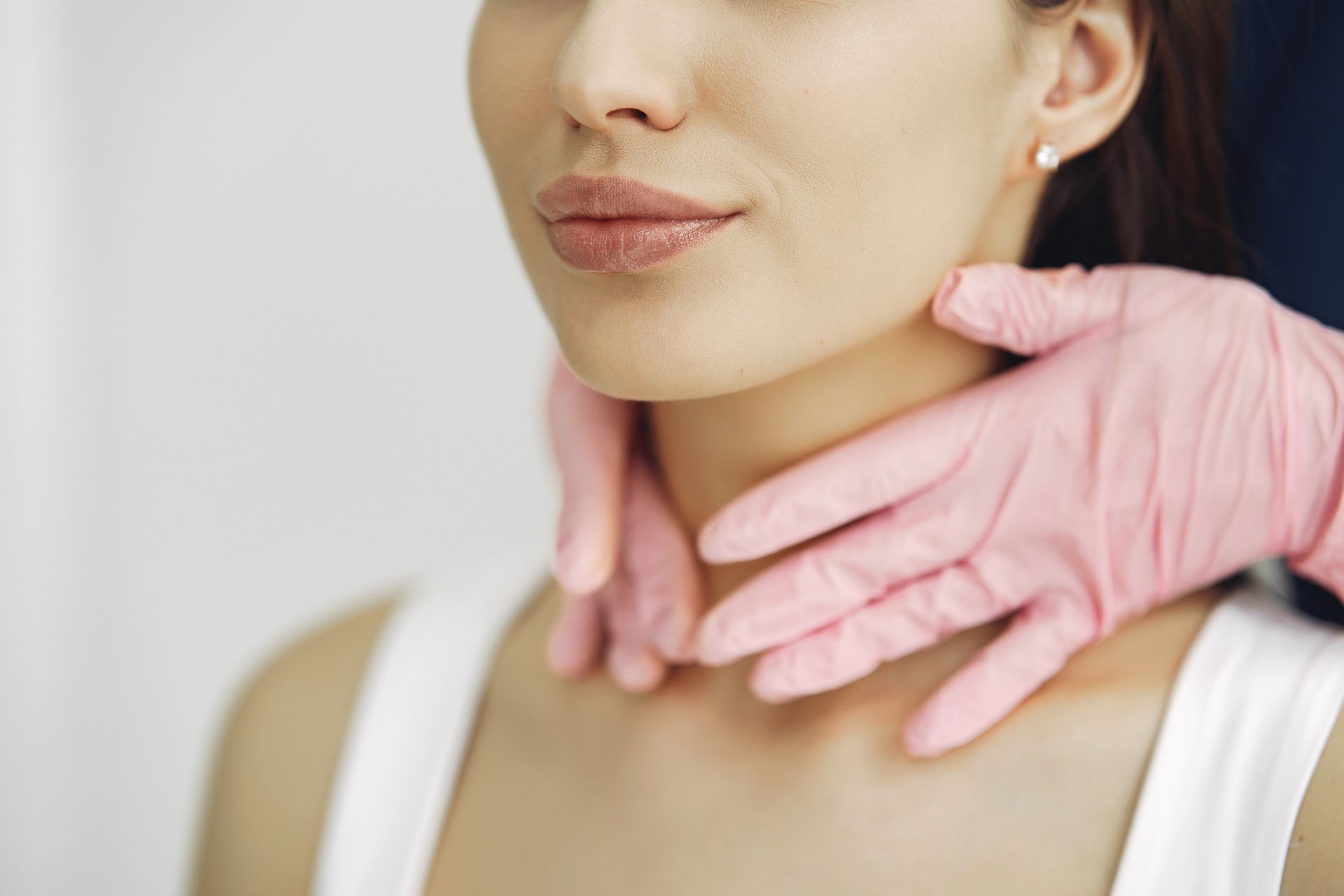 A woman is getting her neck examined by a doctor wearing pink gloves.