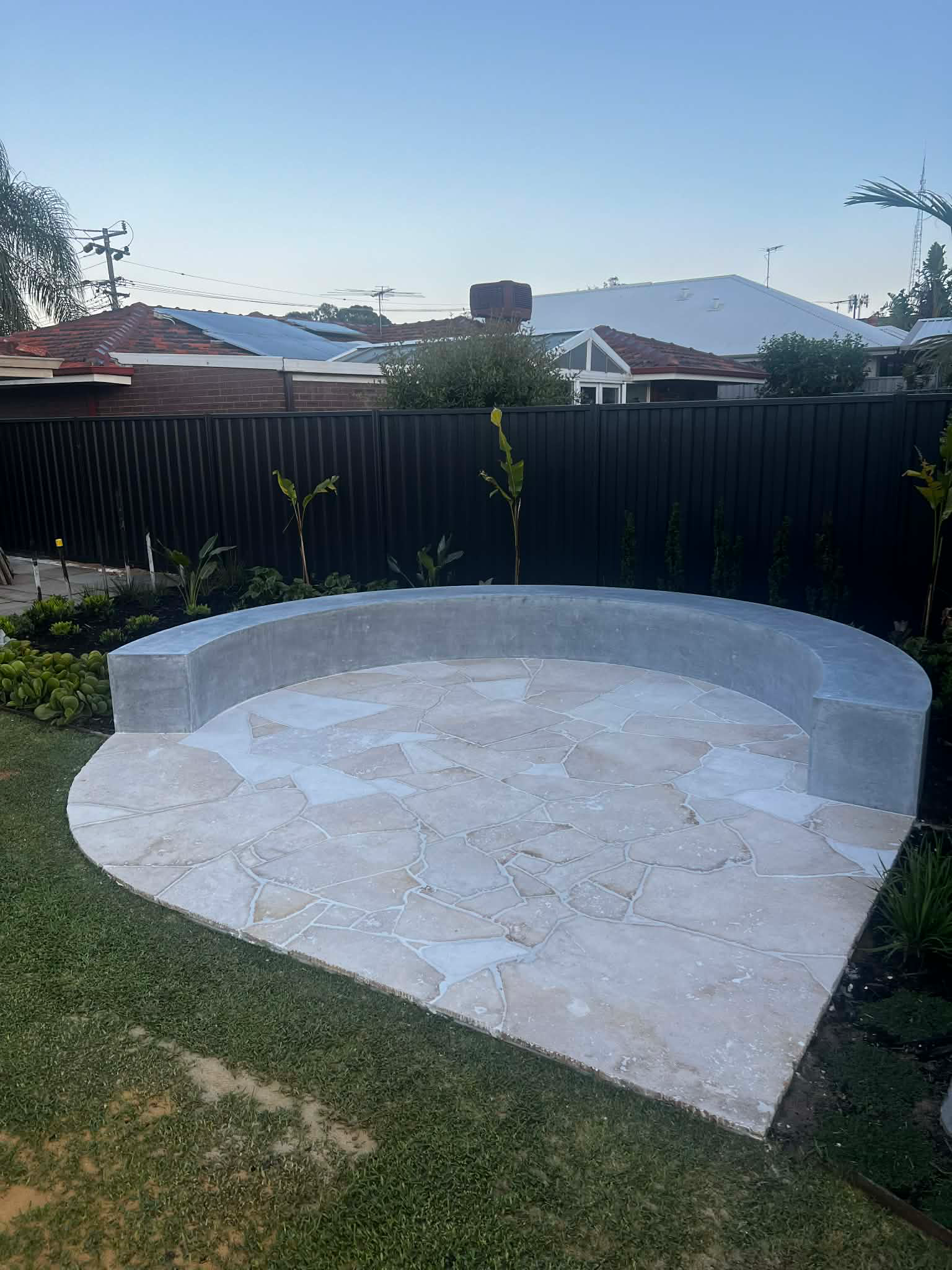 Architectural bench seat finished for fire pit with grey concrete slab for crazy pave on top by Woodlands Construct in Perth homes backyard