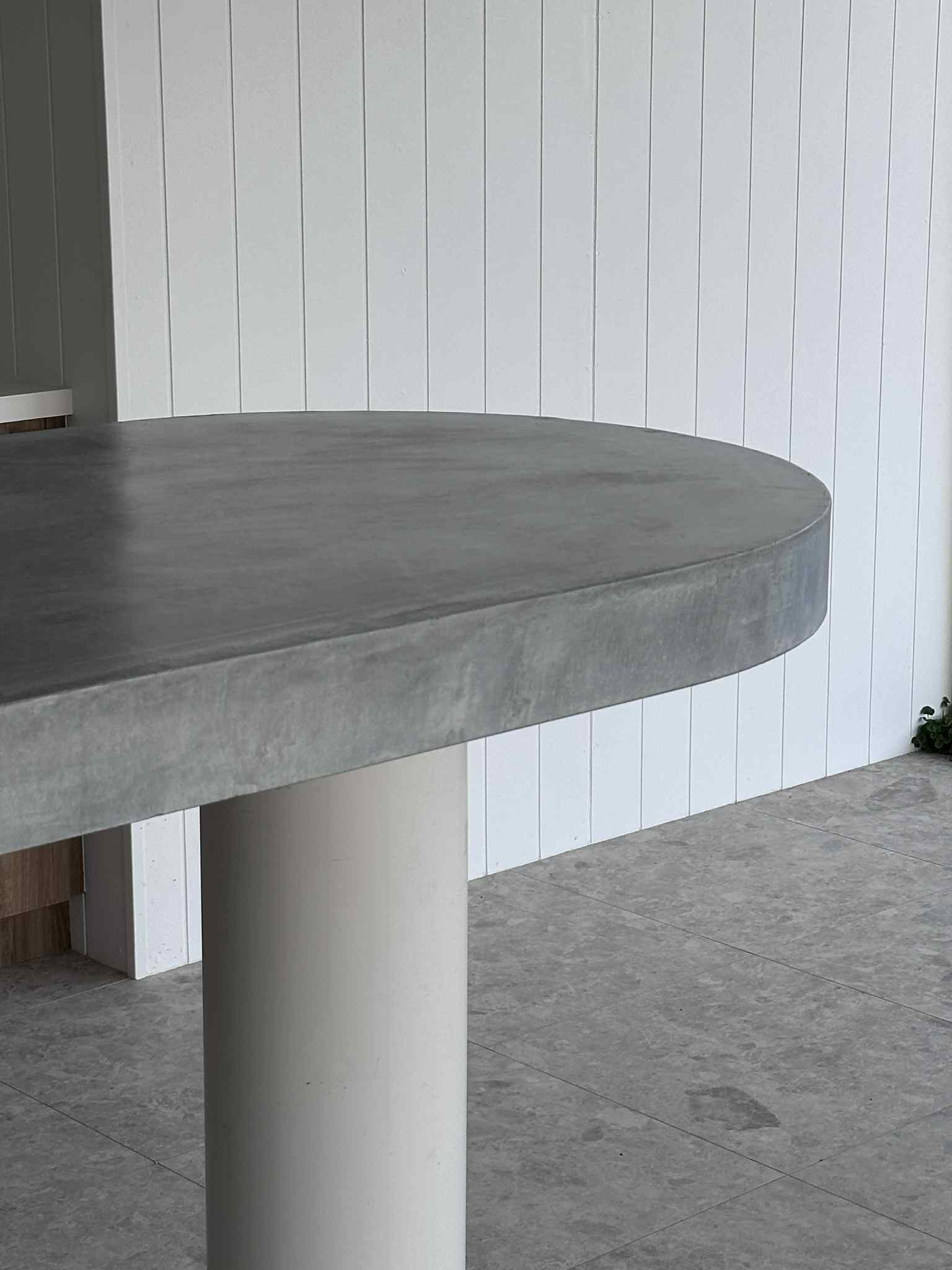 Gray concrete table with white cylindrical base, white vertical panel wall background.