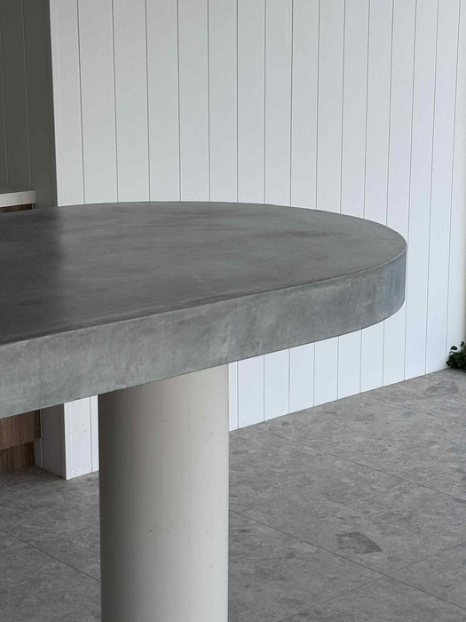 Gray concrete table with white cylindrical base, white vertical panel wall background.