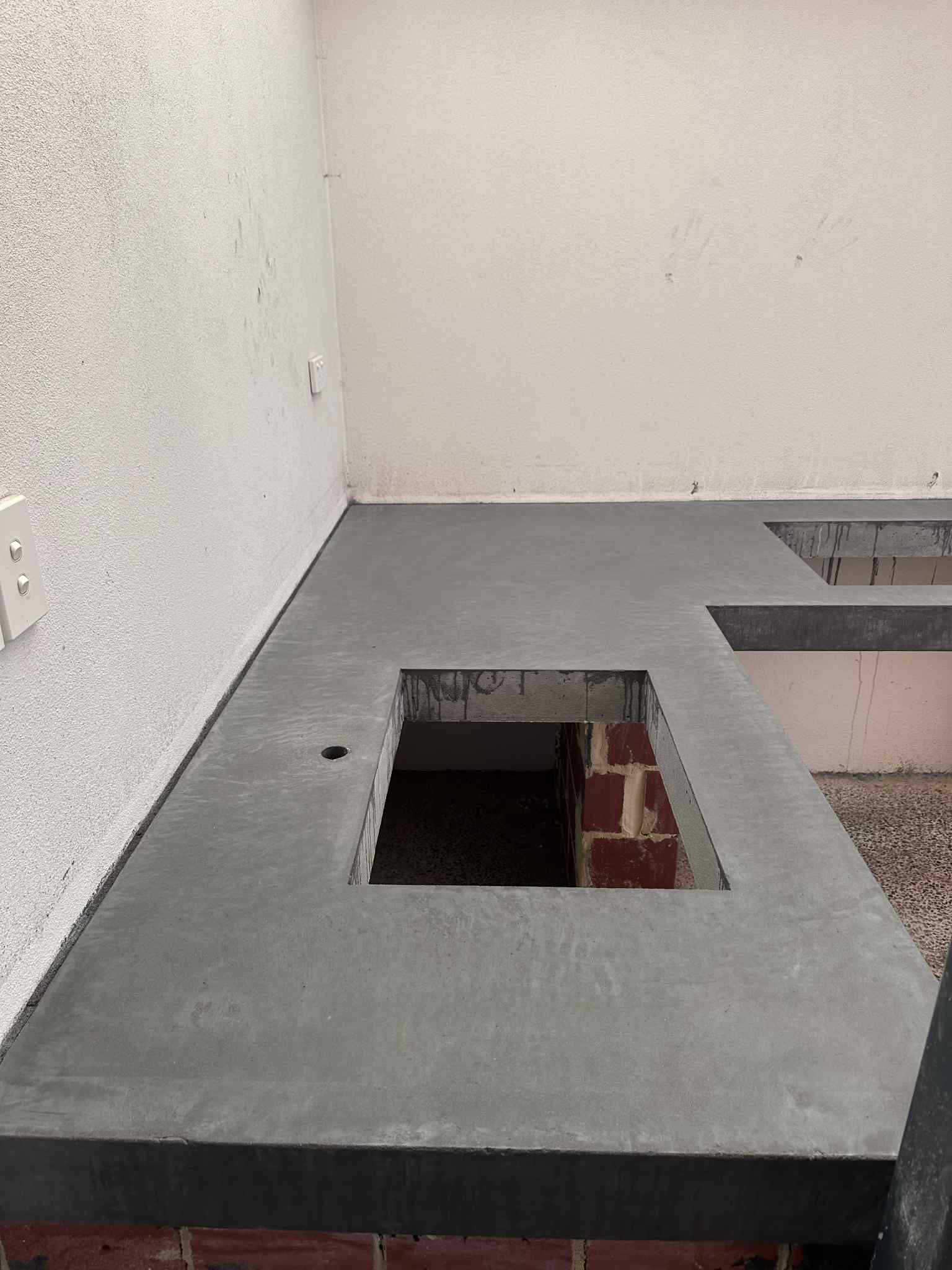 Gray concrete outdoor countertop with cutouts over brick supports, against white walls.