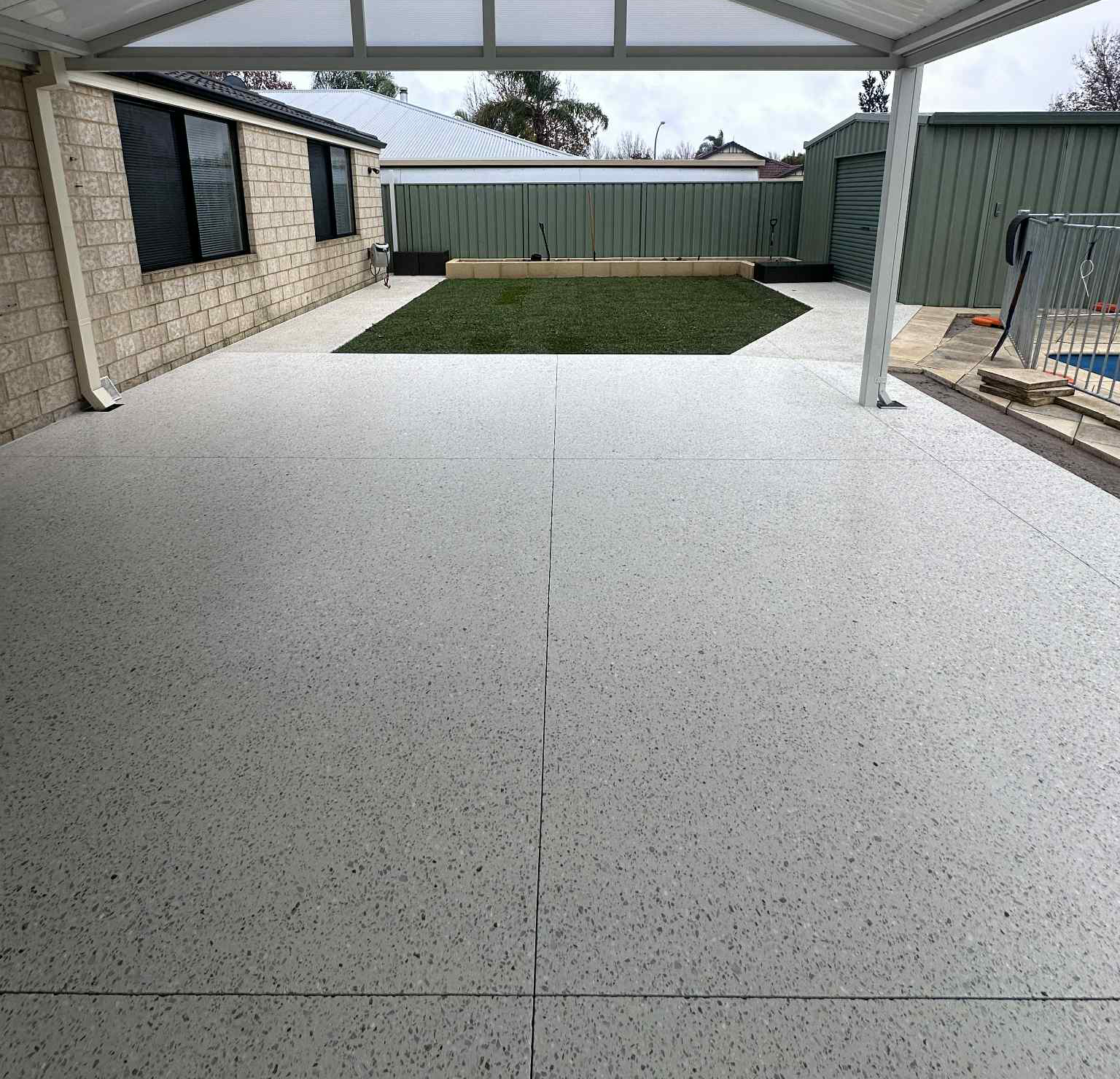 Concrete patio with honed speckled finish under a carport roof, with lawn area in the background.