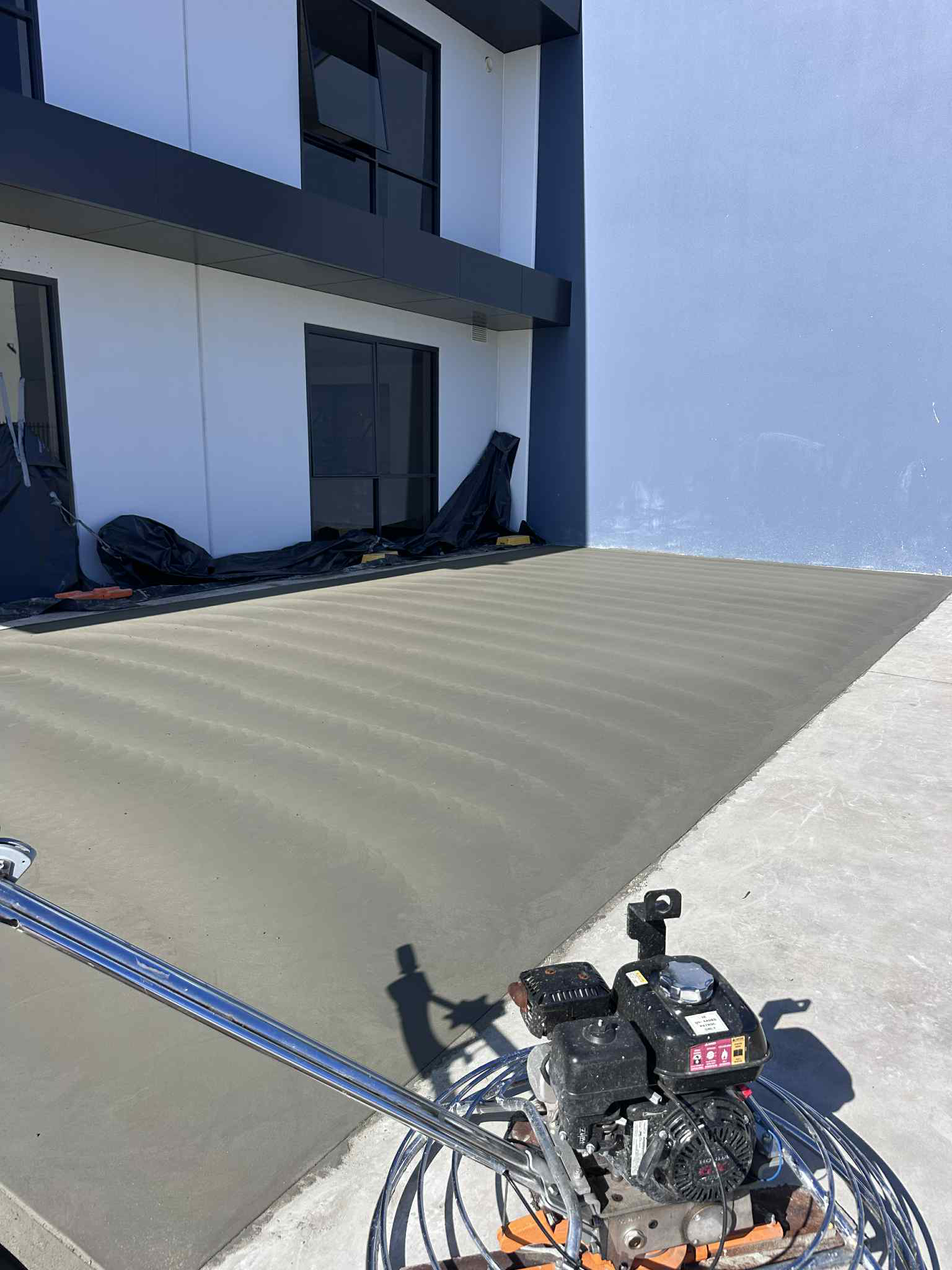 A concrete floor being finished with a power trowel outside a commercial building.
